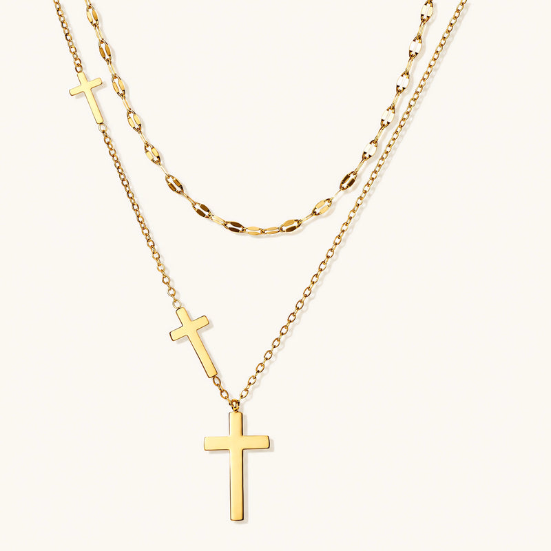 Three-layered gold necklace set with graduated cross pendants in mixed chain styles on white background.